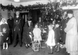 7th January 1927. The Lord Mayor, Alderman Hugh Lupton, and the Lady Mayoress, Ella Lupton, wearing their chains of office, attend a Christmas Party organised for the young residents of Meanwood Park Hospital or 'Colony' as it was then known. Here, a huge christmas tree has been festooned with fairy lights and ornaments, and a frieze of evergreen branches decorates the walls. The Lady Mayoress is taking an interest in a little girl and her dolls pram and there are various other toys beneath the Christmas Tree. The Matron of Meanwood Park Colony in 1927 was Miss Georgina Langdown.